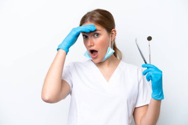 Beyaz arka planda izole edilmiş aletler tutan beyaz dişçi kadın yan tarafa bakarken sürpriz jest yapıyor.