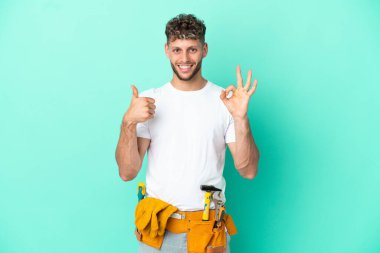 Genç elektrikçi sarışın adam yeşil arka planda izole edilmiş. İşaret ve işaret gösteriyor.