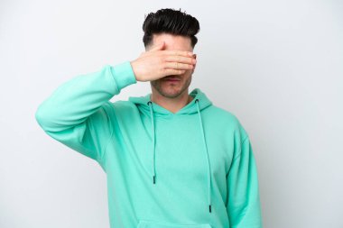 Beyaz arka planda izole edilmiş beyaz tenli genç bir adam gözlerini elleriyle kapatıyor. Bir şey görmek istemiyorum.