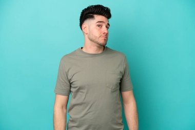 Mavi arka planda izole edilmiş genç beyaz adam şüpheli hareketler yapıyor.