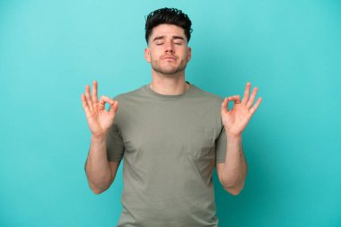 Zen pozisyonunda mavi arka planda izole edilmiş genç beyaz bir adam.