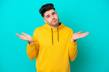 Mavi arka planda izole edilmiş genç beyaz adam ellerini kaldırırken şüpheye düşüyor.