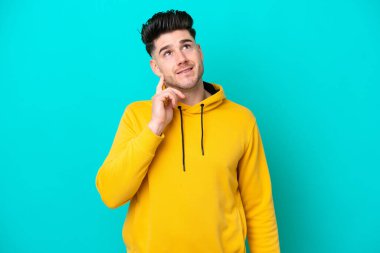 Kafkasyalı genç adam mavi arka planda izole edilmiş bir şekilde yukarı bakarken bir fikir düşünüyor.