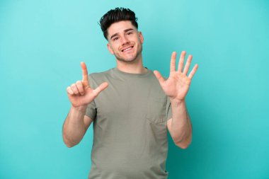 Mavi arka planda izole edilmiş genç beyaz adam yediyi parmaklarıyla sayıyor