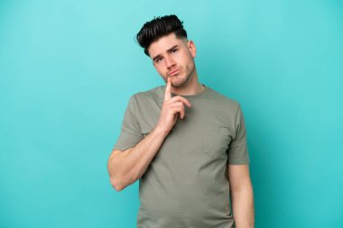 Kafkasyalı genç adam mavi arka planda izole edilmiş ve düşünüyor.