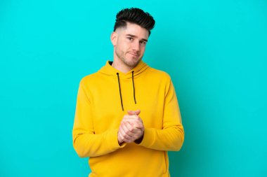 Kafkasyalı genç adam mavi arka planda tek başına gülüyor.