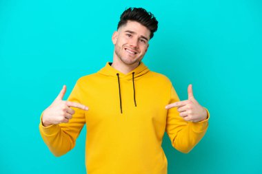 Kafkasyalı genç adam mavi arka planda soyutlanmış gururlu ve kendini beğenmiş.