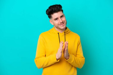 Mavi arka planda izole edilmiş genç beyaz adam bir konferansta sunumdan sonra alkışlıyor.