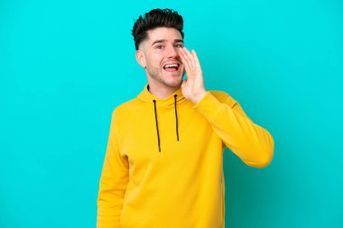 Mavi arka planda izole edilmiş genç beyaz adam ağzı açık bağırıyor.