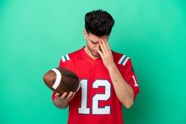 Rugby oynayan genç beyaz adam, yeşil arka planda izole edilmiş, yorgun ve hasta bir ifadeyle.