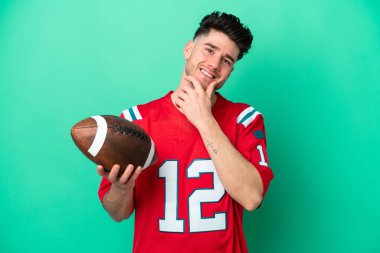 Rugby oynayan genç beyaz adam yeşil arka planda izole edilmiş mutlu ve gülümsüyor.