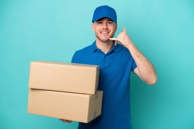 Teslimatçı beyaz adam mavi arka planda izole edilmiş, telefon jesti yapıyor. Bana geri dönüş işareti ver.