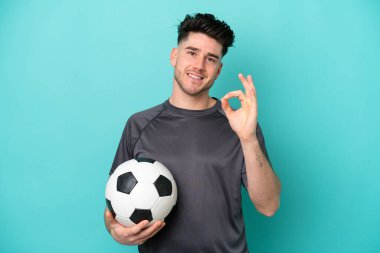 Kafkasyalı genç adam mavi arka planda futbol topuyla izole edilmiş ve 