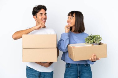 Genç çift, beyaz arka planda izole edilmiş eşyalarla dolu bir kutuyu alıp birbirlerine bakarken hamle yapıyorlar.