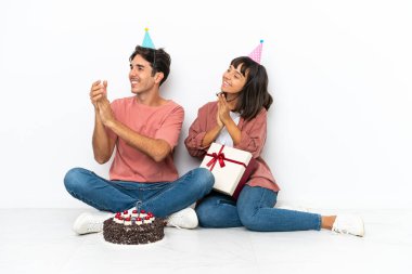 Genç melez çift, bir doğum gününü kutluyorlar. Beyaz arka planda izole bir şekilde oturuyorlar. Bir konferanstan sonra alkış tutuyorlar.