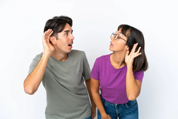 Młoda Para Odizolowana Białym Tle Słuchając Czegoś Kładąc Rękę Uchu — Zdjęcie stockowe