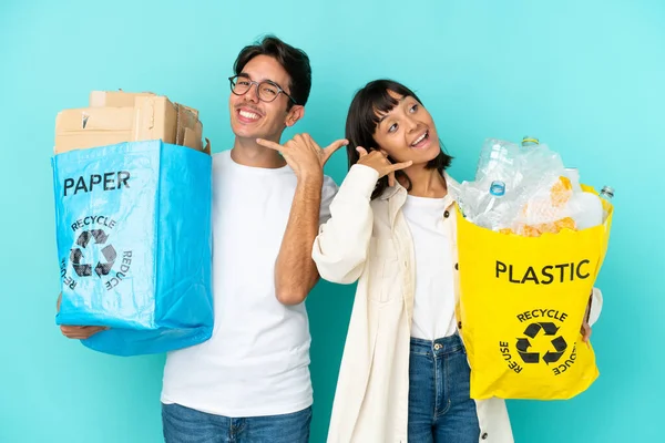 Young couple holding a bag full of plastic and paper to recycle isolated on blue background making phone gesture. Call me back sign