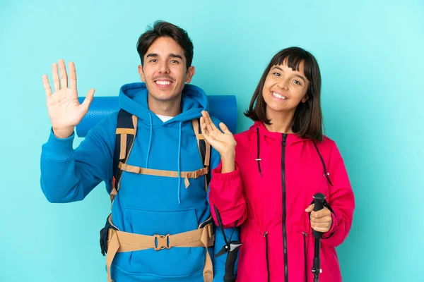 Pareja Jóvenes Montañeros Aislados Sobre Fondo Azul Saludando Con Mano —  Fotos de Stock