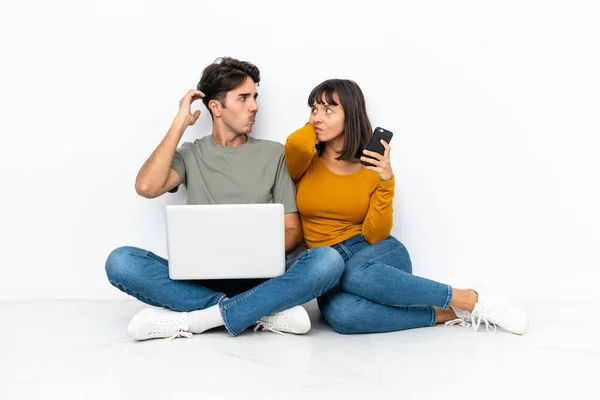 年轻的一对夫妇 带着笔记本电脑和手机坐在地板上疑神疑鬼 抓着头 — 图库照片