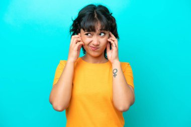 Arjantinli genç bir kadın mavi arka planda izole edilmiş hayal kırıklığına uğramış ve kulaklarını kapatmış