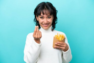 Arjantinli genç bir kadın elinde kızarmış cipslerle mavi arka planda para hareketi yapıyor.