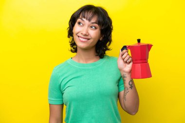 Arjantinli genç bir kadın kahve makinesini sarı arka planda izole edip gülümserken yukarı bakıyor.