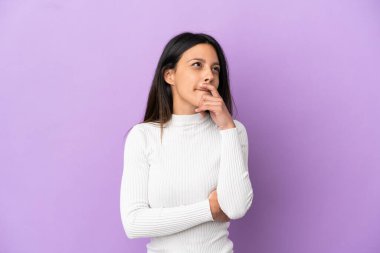 Mor arka planda izole edilmiş genç beyaz bir kadın. Şüpheleri var ve kafası karışmış bir yüz ifadesi var.