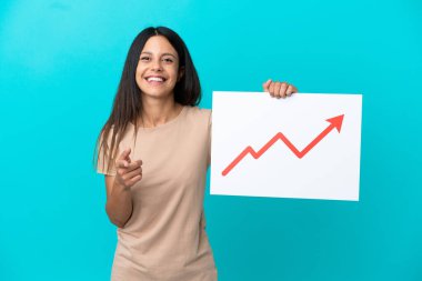 İzole edilmiş arka plan üzerinde büyüyen bir istatistik ok sembolü olan bir tabela tutan ve ön tarafı işaret eden genç bir kadın.