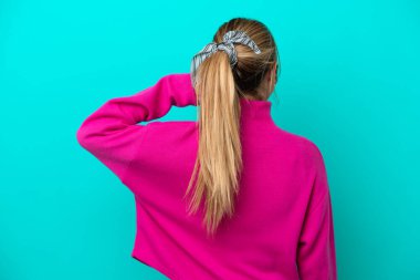 Kafkasyalı genç bir kadın mavi arka planda izole edilmiş ve düşünüyor.