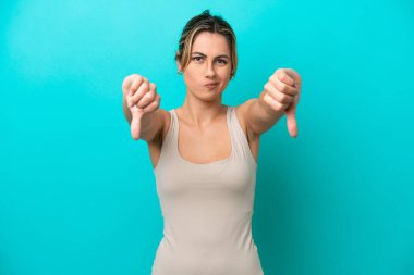 Mavi arka planda izole edilmiş beyaz bir kadın baş parmağını iki eliyle aşağı gösteriyor.