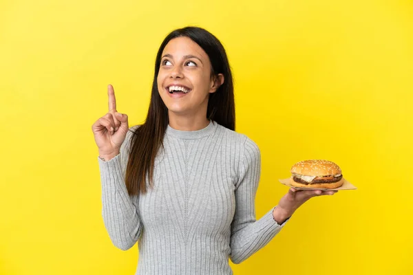 Młoda Kaukaska Kobieta Trzyma Hamburgera Żółtym Tle Wskazując Świetny Pomysł — Zdjęcie stockowe