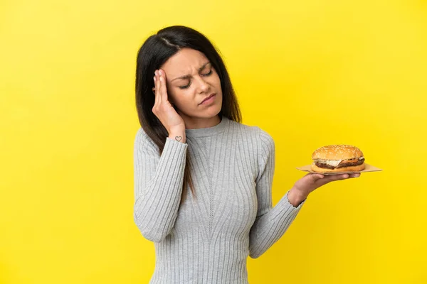 Young Caucasian Woman Holding Burger Isolated Yellow Background Headache — Stock Photo, Image