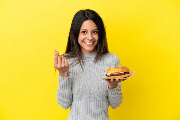 Young Caucasian Woman Holding Burger Isolated Yellow Background Making Money — Stock Photo, Image