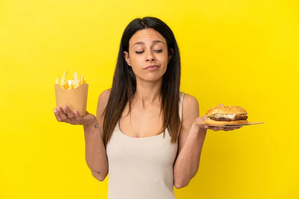 Junge Kaukasische Frau Hält Burger Und Chips Isoliert Auf Gelbem — Stockfoto