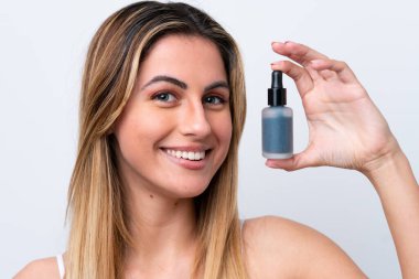 Beyaz arka planda izole edilmiş beyaz bir kadın elinde bir serum tutarken gülümsüyor. Portreyi kapat