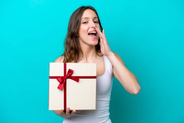 Elinde mavi arka planda ağzı açık bağıran bir hediye tutan beyaz bir kadın.