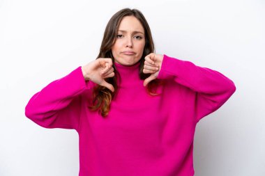 Beyaz arka planda izole edilmiş genç beyaz kadın baş parmağını iki eliyle aşağı gösteriyor.