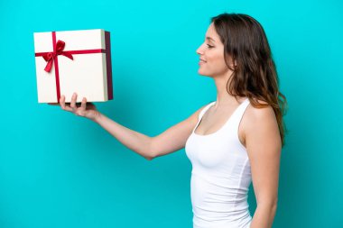 Elinde mavi arka planda mutlu bir ifadeyle izole edilmiş bir hediye tutan beyaz bir kadın.