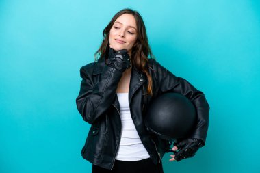 Mavi arka planda izole edilmiş motosiklet kasklı beyaz bir kadın yan tarafa bakıyor ve gülümsüyor.