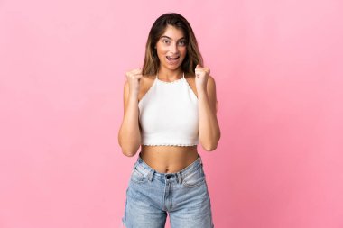 Pembe arka planda izole edilmiş genç beyaz kadın galibiyeti kutluyor.