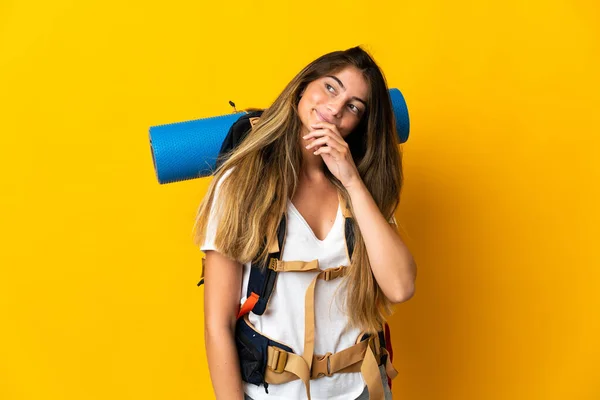 黄色の背景に隔離された大きなバックパックを持つ若い登山家の女性と検索アップ — ストック写真