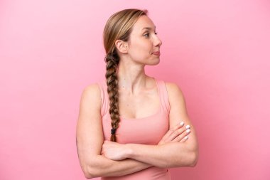 Pembe arka planda izole edilmiş genç beyaz kadın yan tarafa bakıyor.