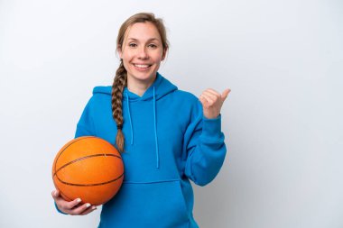Basketbol oynayan beyaz arka planda izole genç beyaz kadın bir ürünü sunmak için kenarı işaret ediyor.
