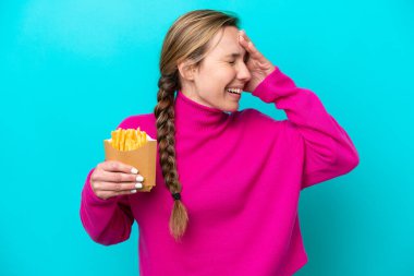 Genç beyaz kadın elinde kızarmış cipslerle mavi arka planda izole edilmiş gülümsüyor.