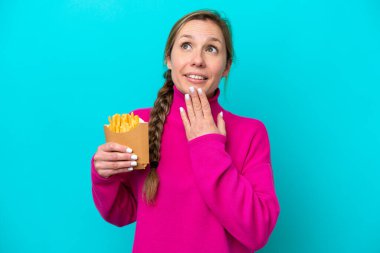 Genç beyaz kadın elinde kızarmış cipslerle mavi arka planda izole edilmiş gülümserken yukarı bakıyor.