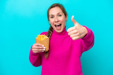 Kafkasyalı genç bir kadın elinde kızarmış cipslerle mavi arka planda izole edilmiş. Başparmakları havada. Çünkü iyi bir şey oldu.