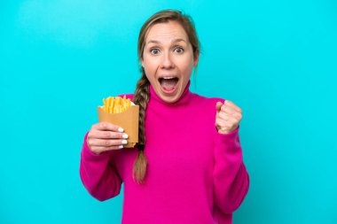 Mavi arka planda kızarmış cips tutan beyaz bir kadın galibiyeti kutluyor.
