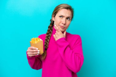 Kafkasyalı genç bir kadın elinde kızarmış cipslerle mavi arka planda kuşkuları var.
