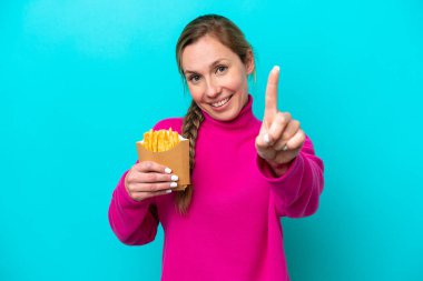 Elinde kızarmış cips tutan beyaz bir kadın mavi arka planda izole edilmiş ve parmağını kaldırıyor.
