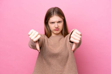 Pembe arka planda izole edilmiş genç Rus kız baş parmağını iki eliyle aşağı gösteriyor.